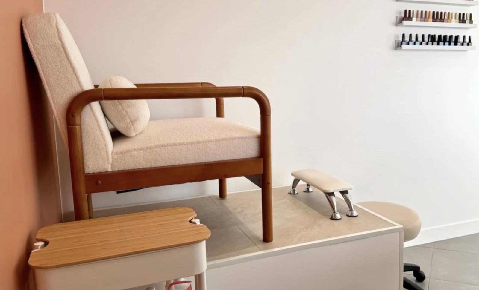 Espace pédicure : fauteuil en bois clair et tissu bouclette, repose-pied et étagères de vernis.